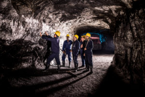 Group of men working at a mine looking at the rock in a dark tunnel- mining concepts